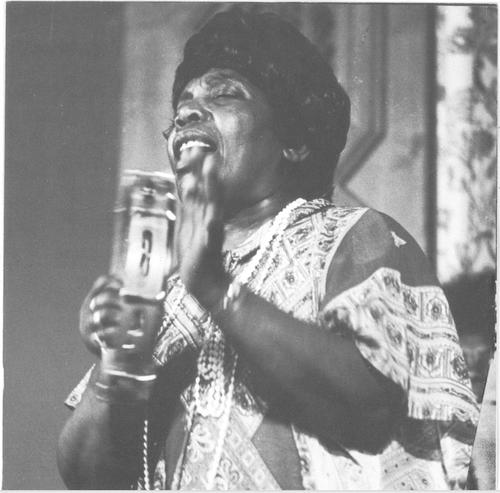 Black and white photo of Bessie Jones holding a microphone and singing