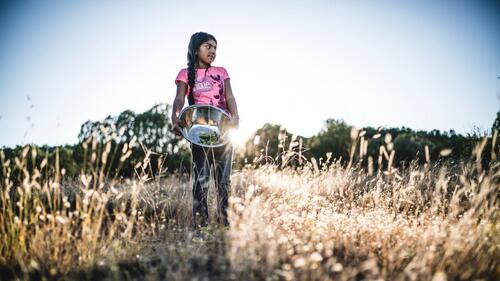 color image of young Apache chef holding a silver bowl in a field from the film Gather