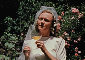 Cynthia Childs in a wedding dress holding a glass of champagne in the film Seductio Ad Absurdum
