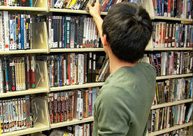 Patron with back to camera examines shelves of videos