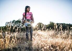 color image of young Apache chef holding a silver bowl in a field from the film Gather
