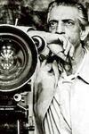 black and white photo of Satyajit Ray standing next to a movie camera